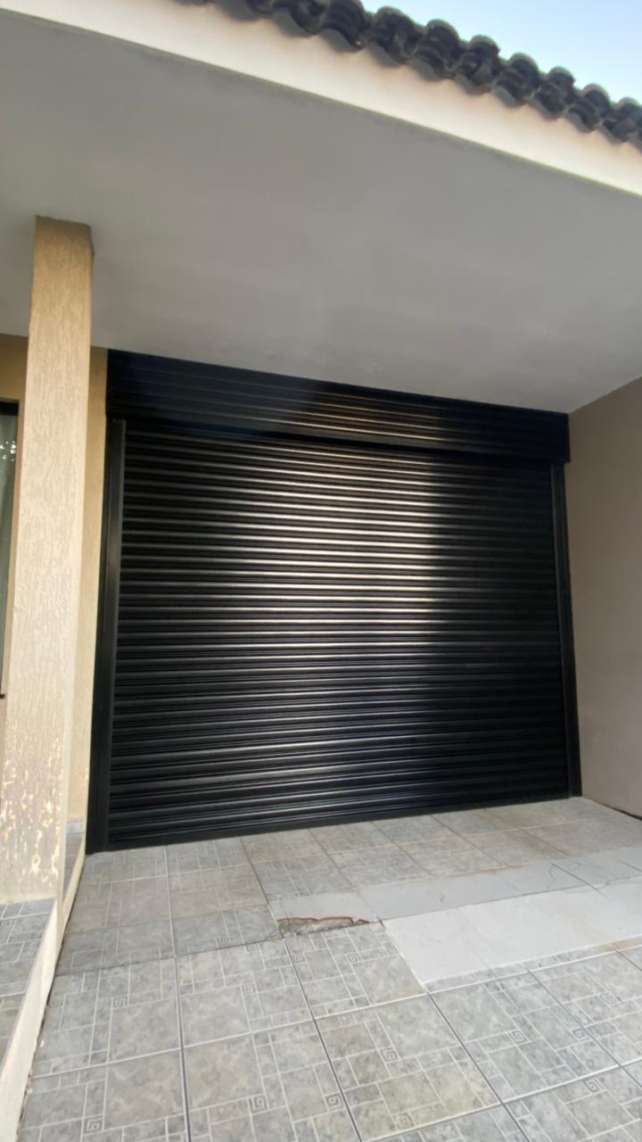 Porta de enrolar preta instalada em garagem coberta de residência