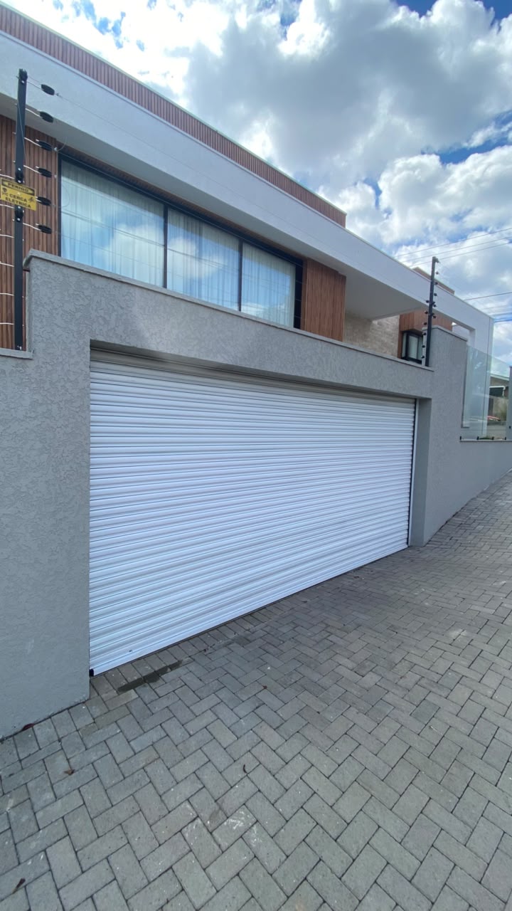 Porta de enrolar branca automatizada instalada em garagem residencial com obra finalizada